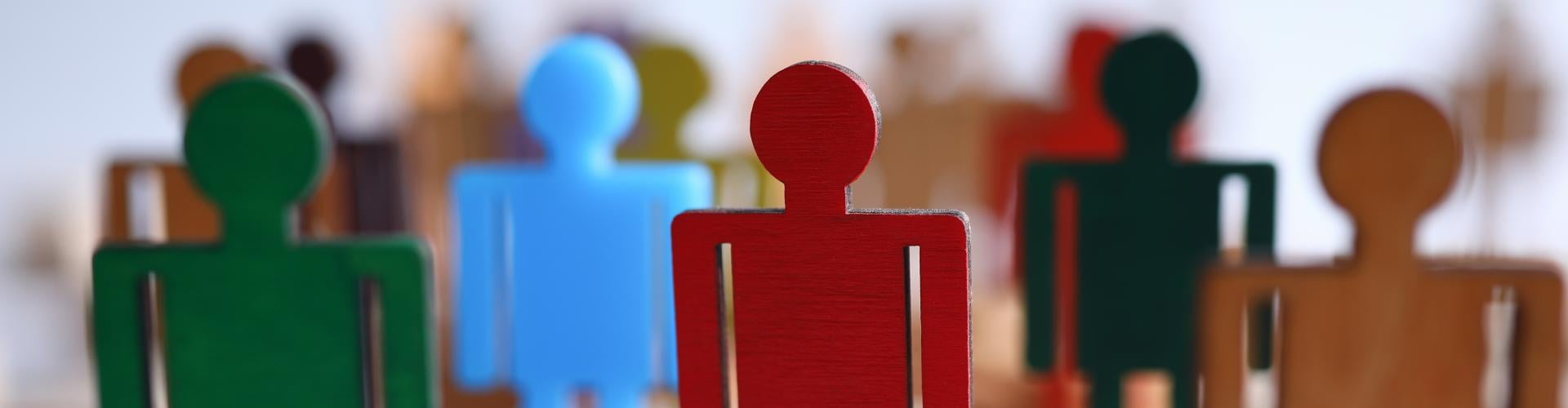Coloured wooden human figures standing on blocks, symbolising leadership, individuality, and diverse representation.