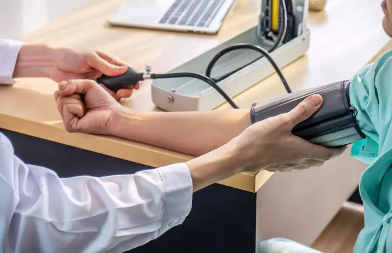 A clinician measuring a patient’s blood pressure with a manual sphygmomanometer — cuff wrapped around the patient’s upper arm and the clinician squeezing the pump while holding the patient’s wrist.